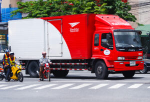 A Thailand post Isuzu truck waits for the train to pass at a level crossing.