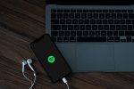 A mobile phone with the Spotify logo, near a MacBook Pro.