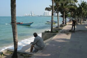 A man sitting down near some boats on Pattaya Beach Road, Thailand.