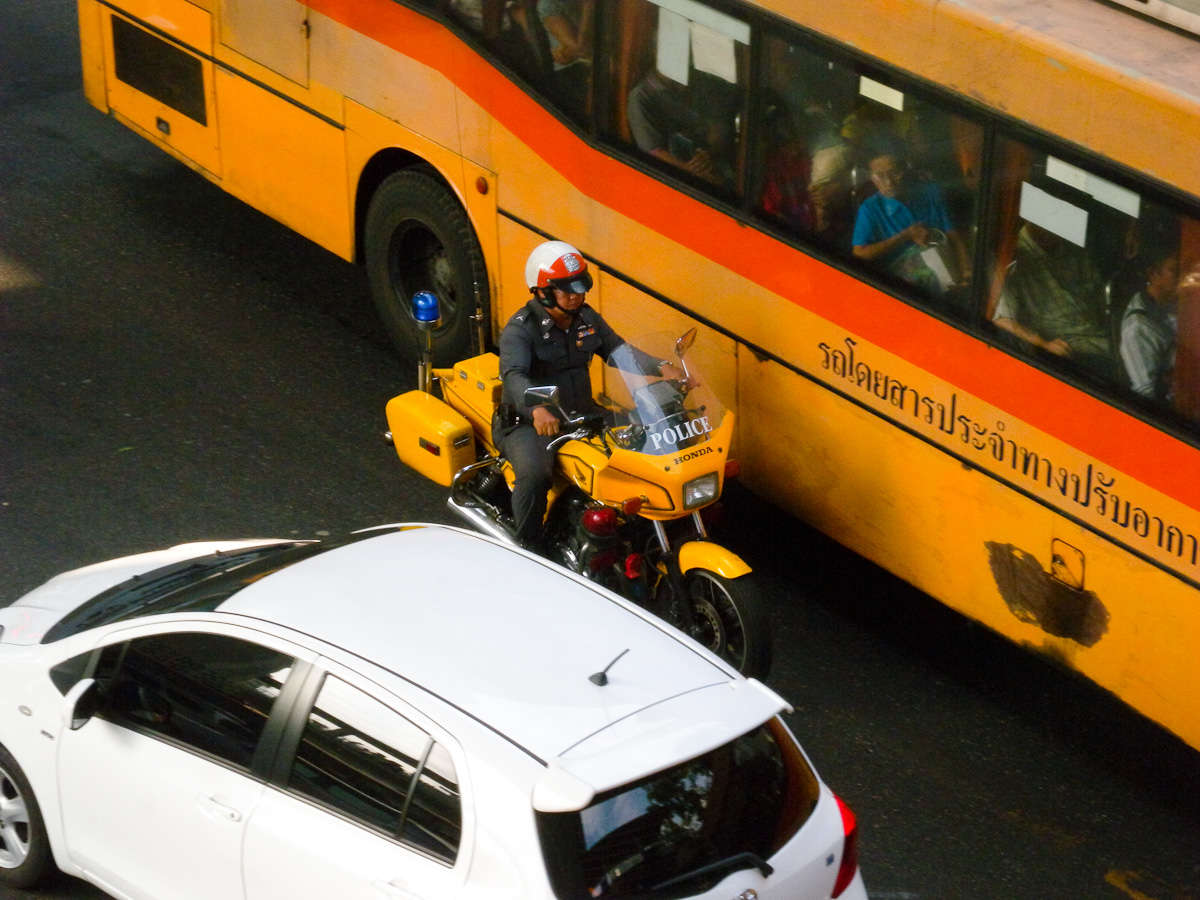 A police officer makes his way through dense traffic near a bus on Bangkok's Rama 1 Road.