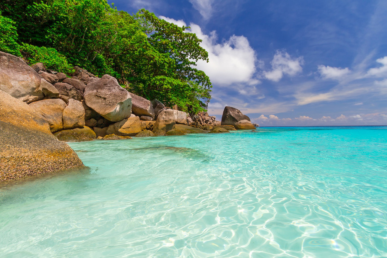 Clear blue waters lined with rocks and trees in the Similan Islands, Thailand.